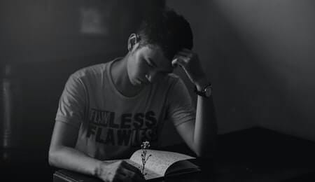 garoto triste em preto e branco lendo um livro na mesa