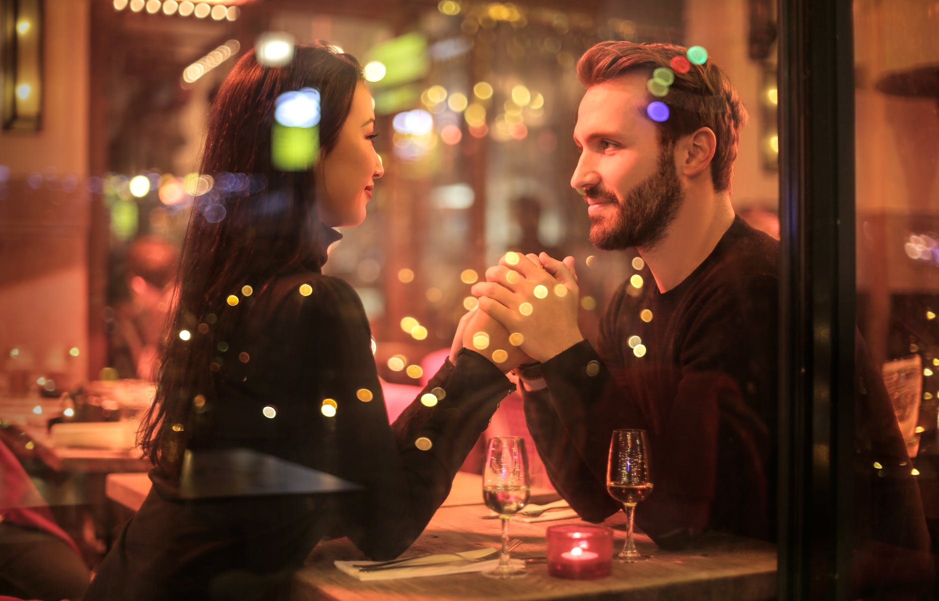 casal sentado de frente um para o outro dentro de um restaurante segurando as mãos enquanto se olham