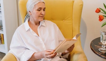 mulher em menopausa lendo um livro sentada na poltrona