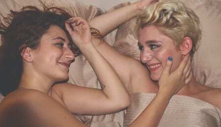 casal de mulheres deitadas na cama nuas olhando uma para a outra e sorrindo