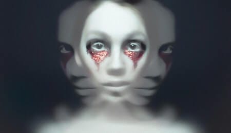 pessoa com maquiagem branca e brilhos vermelhos ao redor dos olhos com a imagem distorcida