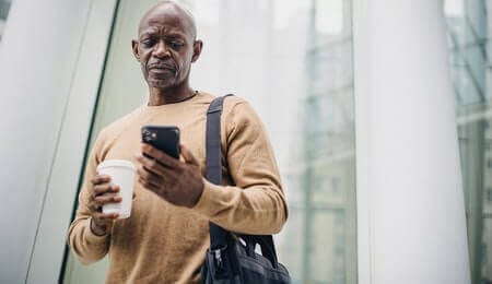 homem negro bebendo um café e olhando seu smartphone na saída do trabalho