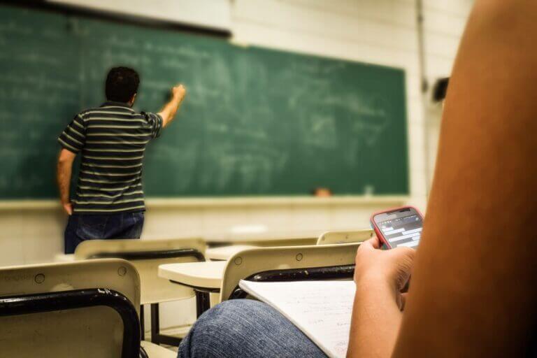 sala de aula com professor escrevendo no quadro e a aluna usando o celular durante a volta às aulas presenciais