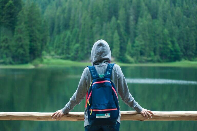 solidão e solitude mochileiro observando um lago de uma ponte de madeira com uma floresta ao fundo