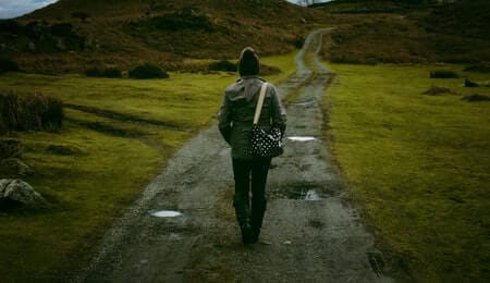 pessoa de costas andando no meio de um caminho de terra em solitude