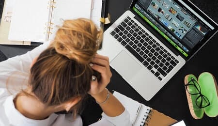 mulher com ansiedade colocando as mãos na cabeça em uma expressão de nervosismo sentada em frente ao seu computador