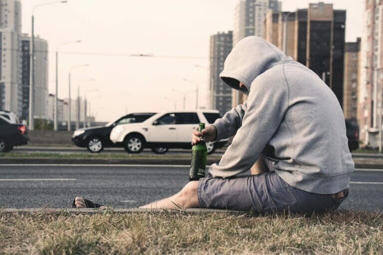 homem sofrendo com o alcoolismo sentado segurando uma garrafa de cerveja