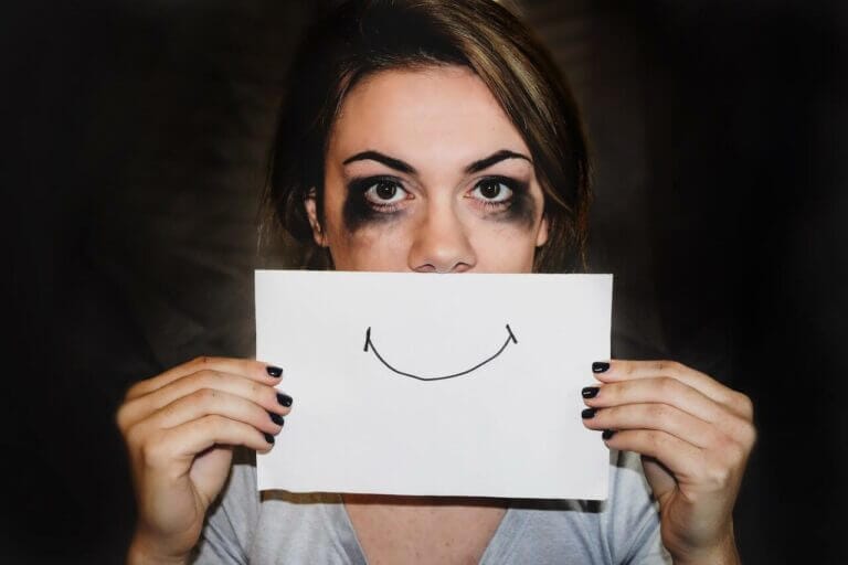 mulher com síndrome da impostora com os olhos manchados de tinta preta enquanto segura um papel com um sorriso desenhado