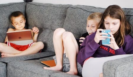 três crianças usando celular e computador fixamente no sofá e como se livrar de um vício assim