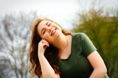 mulher de camisa verde sorrindo feliz por vencer a síndrome do impostor