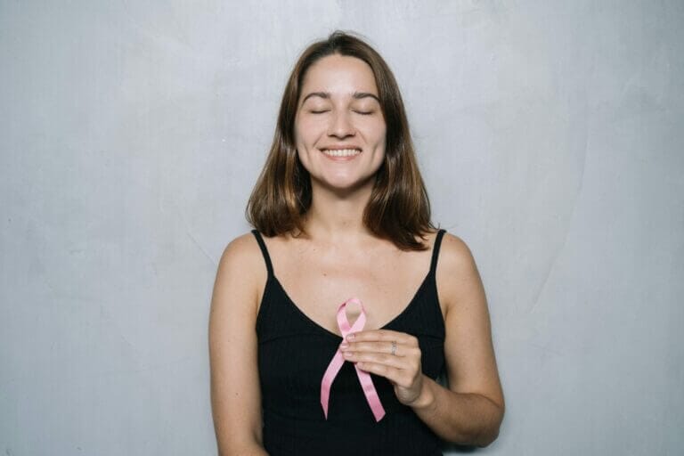 mulher de top preto segurando um laço rosa simbolizando a importância da mamografia e luta contra o câncer de mama