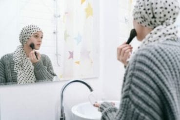 mulher com lenço passando maquiagem representando a saúde mental dos pacientes com câncer de mama