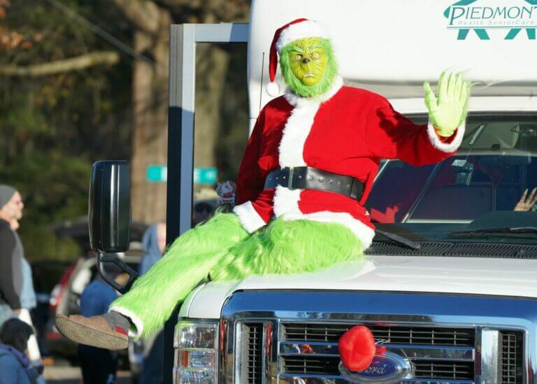 Grinch com roupa de natal sentado em cima de carro para representar a síndrome de grinch