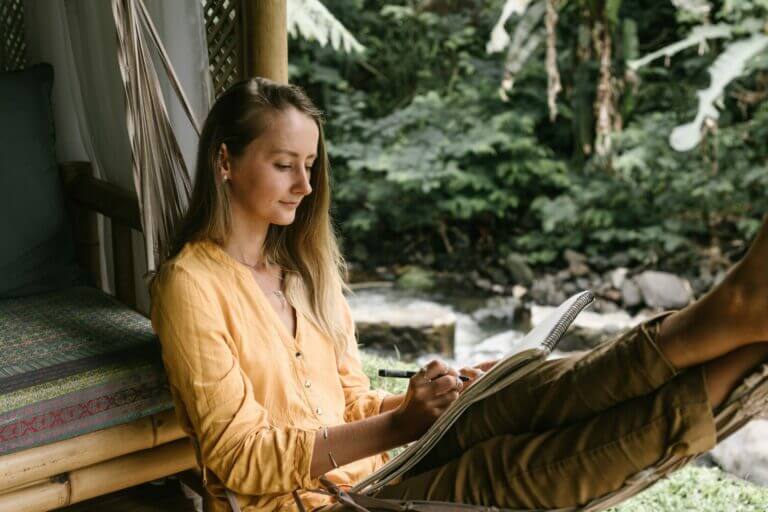 mulher sentada na natureza enquanto escreve mostrando como ter férias produtivas