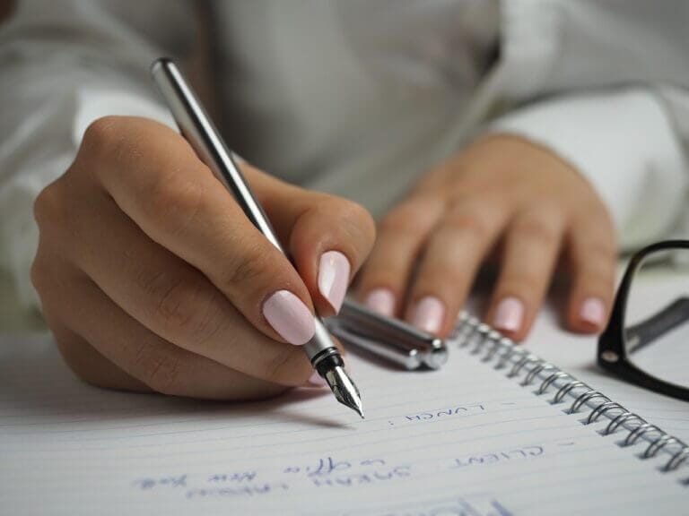 mulher escrevendo na agenda com caneta depois aprender como fazer uma autoavaliação