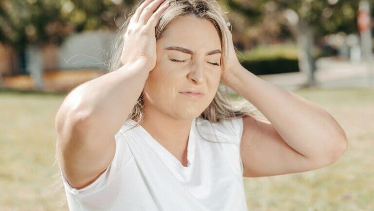 mulher com as mãos na cabeça sentindo dor por causa de fatores emocionais