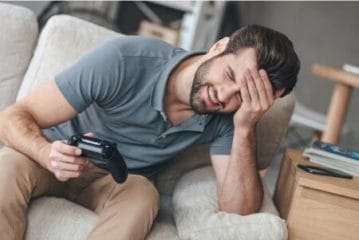 homem segurando controle de videogame e sentindo dores de cabeça após jogar em excesso